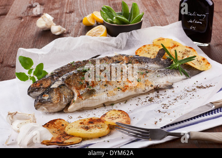 Deux truites grillées sur plaque blanche avec des morceaux de citron, pomme et balsamico sur essuie-tout sur table en bois. Banque D'Images