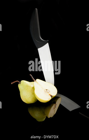 Morceau de poire et couteau en céramique noir et blanc isolé sur fond noir. En bonne santé luxe fruits d'été. Banque D'Images