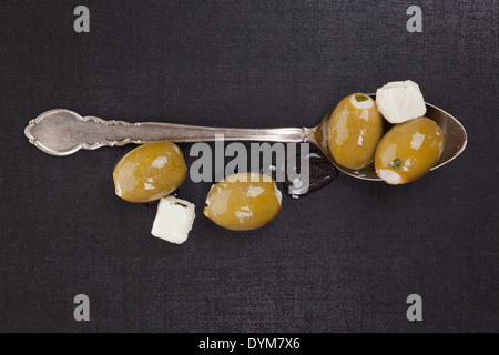 Olives vertes de fromage sur argent vintage cuillère sur fond noir et gris foncé, vue du dessus. Luxueux sain culinaire Banque D'Images