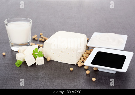 Les produits de soja. Le tofu, lait de soja, le soja, la sauce de soja et la crème de soja sur fond gris foncé et noir. L'alimentation végétarienne et végétalienne. Banque D'Images
