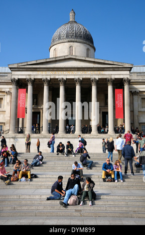 Londres, Angleterre, Royaume-Uni. Des gens assis sur les marches de la National Gallery à Trafalgar Square Banque D'Images