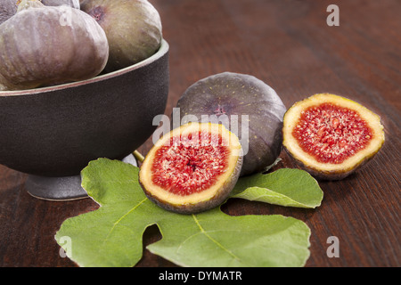 De délicieuses figues fraîches avec feuille verte isolée sur fond de bois brun. Des fruits sains de manger. Banque D'Images