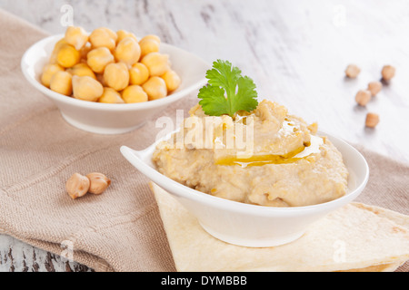 L'hummus délicieux cuit et les pois chiches dans un bol blanc sur fond de bois. L'hummus culinaire méditerranéenne de manger, de style rustique. Banque D'Images