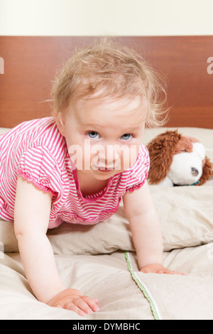 Cute adorable petite fille de 12 mois avec de grands yeux bleus sur le lit avec son jouet préféré à la recherche en appareil photo. Banque D'Images