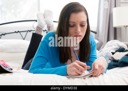 Teenage girl writing in journal ou cahier on bed Banque D'Images