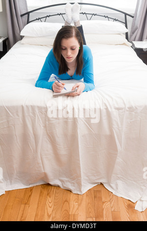 Teenage girl writing in journal ou cahier on bed Banque D'Images