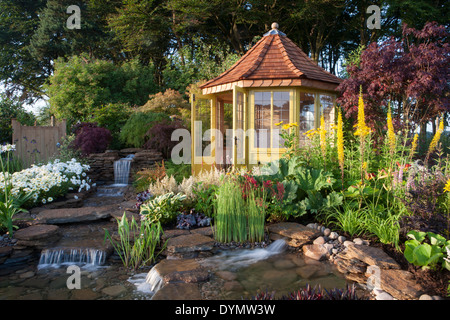Un jardin de banlieue de campagne en été avec une maison d'été chalet petite piscine d'eau avec chute d'eau et frontière de fleur colorée mixte Royaume-Uni Banque D'Images