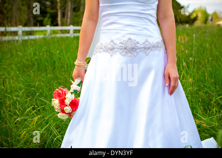 Promise dans son robe de mariée blanche tenant un beau bouquet de fleurs roses notamment. Banque D'Images