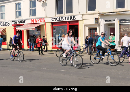 Visiteurs à participer à la ronde du cycle traditionnel de l'île de (Cumbrae). Dans l'arrière-plan est un service de location de vélos et Mapes toy shop à Millport, Ecosse, Royaume-Uni Banque D'Images