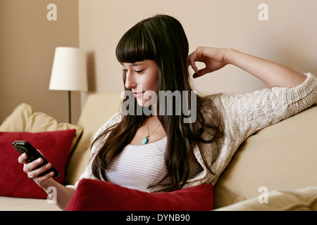 Mixed Race woman using cell phone on sofa Banque D'Images