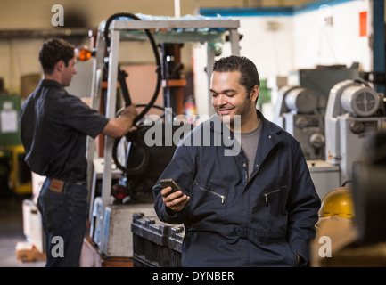 Travailleur using cell phone in warehouse Banque D'Images