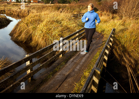 Caucasian woman jogging le pont de bois sur creek Banque D'Images