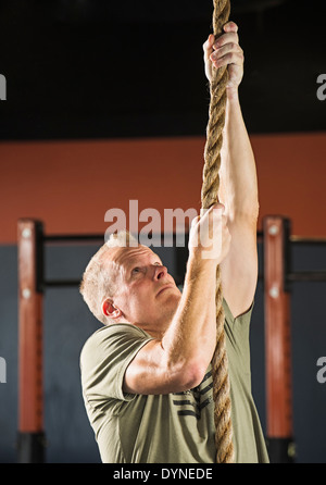 Caucasian man climbing rope in gym Banque D'Images