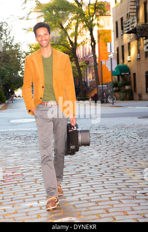 Mixed Race man carrying guitar on city street Banque D'Images