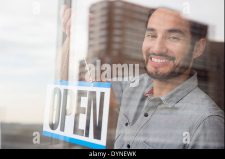 Mixed Race man placing Open sign in shop window Banque D'Images