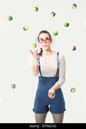 Young hispanic woman concentré avec des lunettes à jongler avec plusieurs balles Banque D'Images