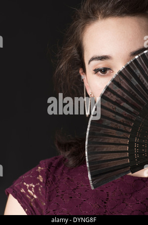 Pensive hispanic woman covering her face avec ventilateur à main pliable Banque D'Images