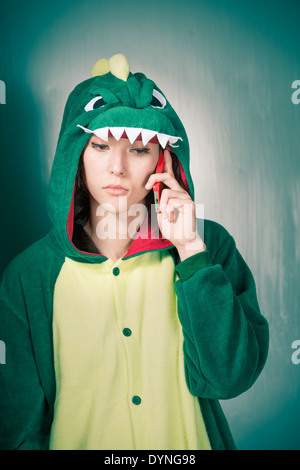 Femme sérieuse en costume de dinosaure holding mobile phone Banque D'Images