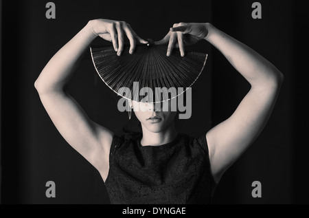 Hispanic woman covering her face avec ventilateur à main pliable Banque D'Images