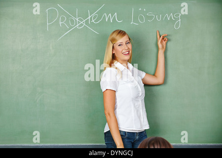 Happy woman pointing to German words pour problème et solution on chalkboard Banque D'Images