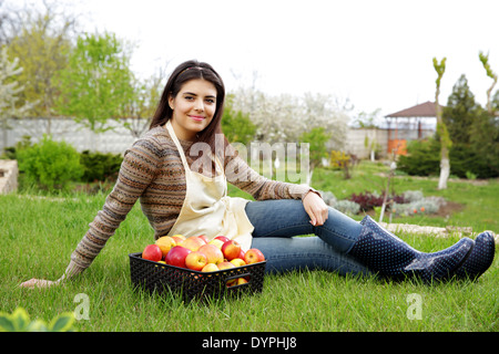 Portrait de femme heureuse avec pommes panier sitting on grass in garden Banque D'Images