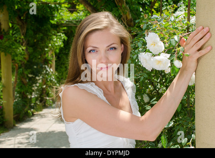 Heureux femme aux cheveux blonds et aux yeux bleus dans le parc sur un fond de fleurs Banque D'Images