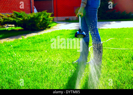 La femme est d'arroser l'herbe dans son jardin Banque D'Images