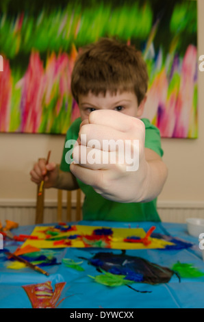 Garçon de huit ans d'art et d'artisanat faire colle ciseaux avec montage et peinture. Faire semblant d'être agressif Banque D'Images