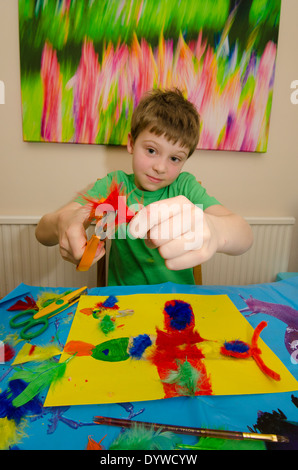 Garçon de huit ans d'art et d'artisanat faire colle ciseaux avec montage et peinture. Banque D'Images