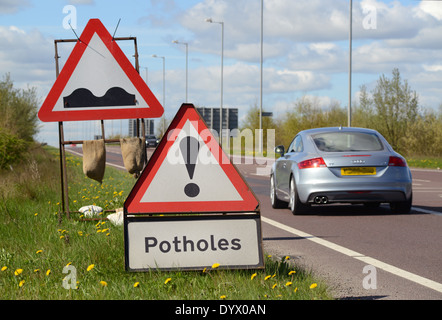 Une voiture passe sur la route des panneaux d'avertissement des fondrières Royaume-Uni Banque D'Images