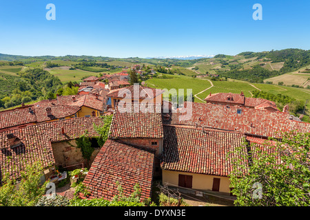 De toits en tuile rouge petit village et collines vertes sous ciel bleu au printemps en Piémont, Italie du Nord. Banque D'Images