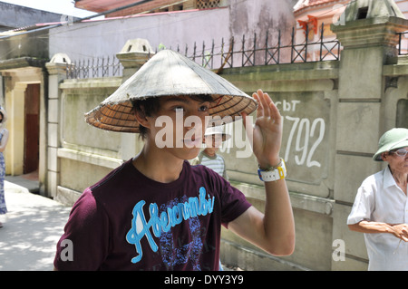 Teenage boy'portant un chapeau conique au Vietnam pour abriter du soleil Banque D'Images