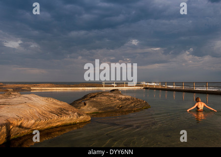 Piscine intégrée dans l'océan mer naturelle-rocks. Photo sur très encore jour avec un seul nageur. nuages de tempête de lumière dorée l'Australie Banque D'Images