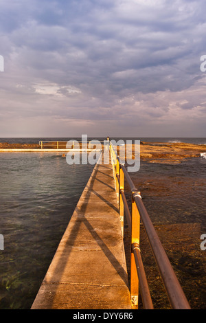 Vue vers le bas de la main courante piscine intégrée dans l'océan mer naturelle-rocks. Encore jour. seul nageur & personne marchant bord de l'Australie Banque D'Images