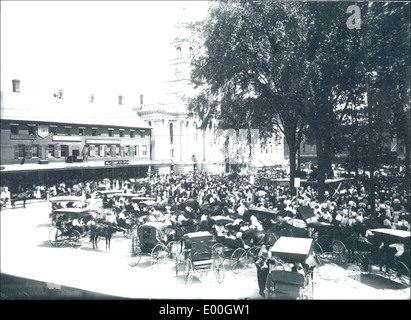 Photographie historique d'un concert à Central Square, Keene, New Hampshire, mettant en vedette des calèches et des buggys tirés par des chevaux de l'époque. Cette image, capturée par Bion Whitehouse, offre un aperçu de la vie au XIXe siècle. Banque D'Images