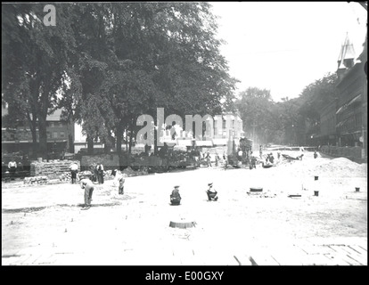 Une photographie historique montrant le processus de pavage de la route à Keene, New Hampshire, autour de Central Square. L'image montre des travailleurs posant de l'asphalte, mettant en évidence le développement de l'infrastructure dans cette ville de Nouvelle-Angleterre. Banque D'Images