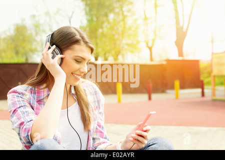 Jeune femme avec un casque et téléphone dans l'écoute de la musique du parc Banque D'Images