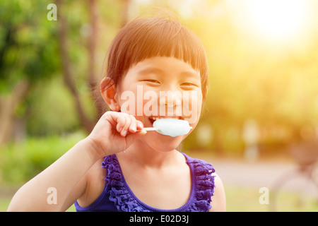 Happy little girl eating popsicle avec fond coucher de soleil Banque D'Images