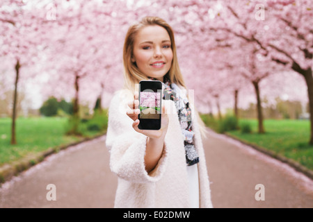 Pretty young woman showing photo de fleur de printemps jardin tout en se tenant à un parc. Les jeunes femmes caucasiennes spring park Banque D'Images