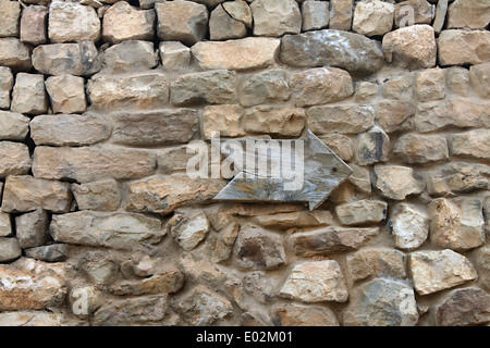 En bois d'une flèche pointant sur un vieux mur de pierre. Banque D'Images