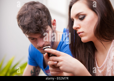 Une belle jeune femme l'envoi de messages texte avec son mobile téléphone malgré son très homme frustré Banque D'Images