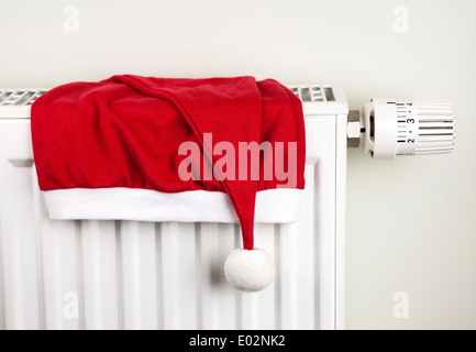 Red Christmas hat placés sur blanc accueil chauffage avec thermostat de radiateur Banque D'Images