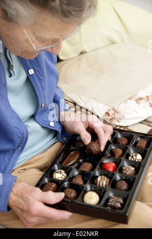 Femme âgée aidant elle-même à un chocolat d'une boîte de chocolats Banque D'Images