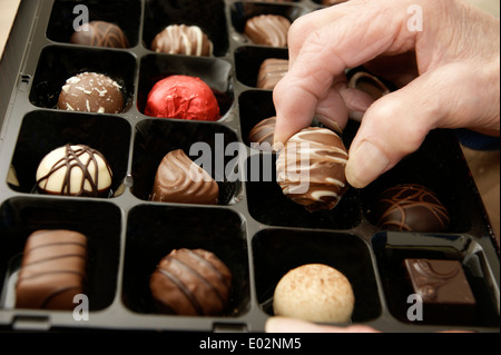 Femme âgée aidant elle-même à un chocolat d'une boîte de chocolats Banque D'Images