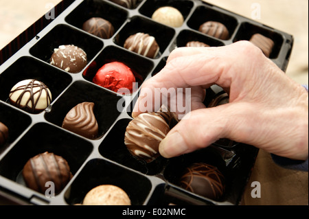 Femme âgée aidant elle-même à un chocolat d'une boîte de chocolats Banque D'Images