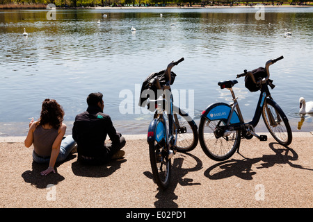 Couple avec Barclays Cycle Hire à Londres au repos des vélos par la Serpentine dans Hyde Park. Banque D'Images