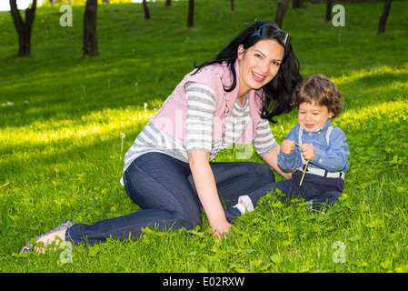 Cheerful mère et petit garçon assis dans l'herbe et s'amuser ensemble Banque D'Images