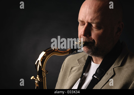 Close up of hot musician playing saxophone ténor les yeux fermés, fond sombre Banque D'Images