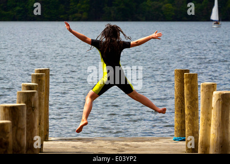 Fillette de douze ans en sautant de wetsuit jetée en bois sur le lac Windermere dans le Lake District National Park Cumbria England UK Banque D'Images