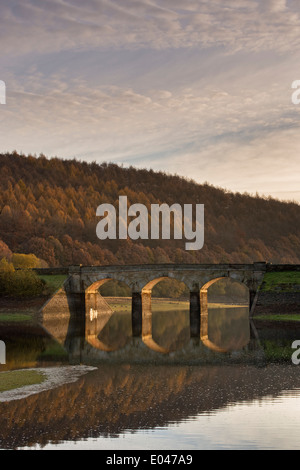 Vue panoramique du pont de la route d'arches ensoleillée & Woodland, reflétée dans l'eau calme de Lindley Wood - près de Otley, North Yorkshire, Angleterre, Royaume-Uni. Banque D'Images